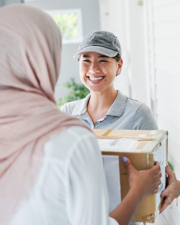 Shot of an attractive young woman standing and delivering a box to a customer at their home.